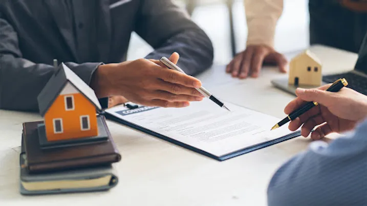 Hands holding pens over a contract next to model house