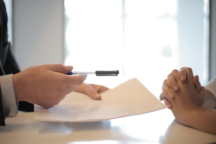 Professional handing a white document and pen to a client