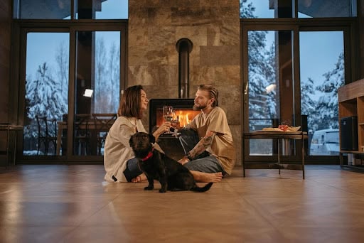 Couple sitting on floor toasting wine glasses by fireplace